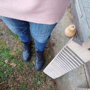 May include: A wooden washboard with a handle, sitting on a concrete surface. The washboard has a worn, rustic look and is made of light wood with dark grooves. A person is holding the handle of the washboard.