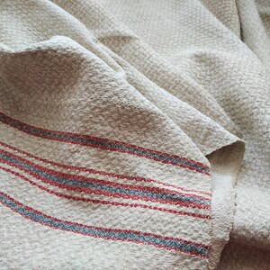 May include: A close-up of a piece of off-white fabric with red and blue stripes. The fabric is wrinkled and has a textured surface.
