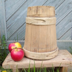 Puede incluir: Un cubo de madera con dos bandas alrededor de la parte superior, sentado en un taburete de madera con dos manzanas rojas delante.