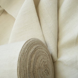 May include: A roll of natural white fabric, unbleached and tightly wound. The fabric is smooth and has a subtle texture.