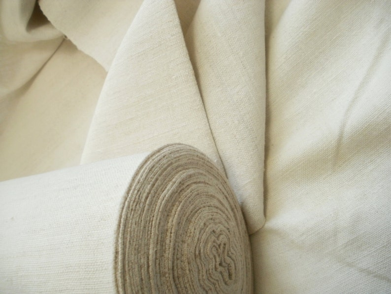 May include: A roll of natural white fabric, unbleached and tightly wound. The fabric is smooth and has a subtle texture.