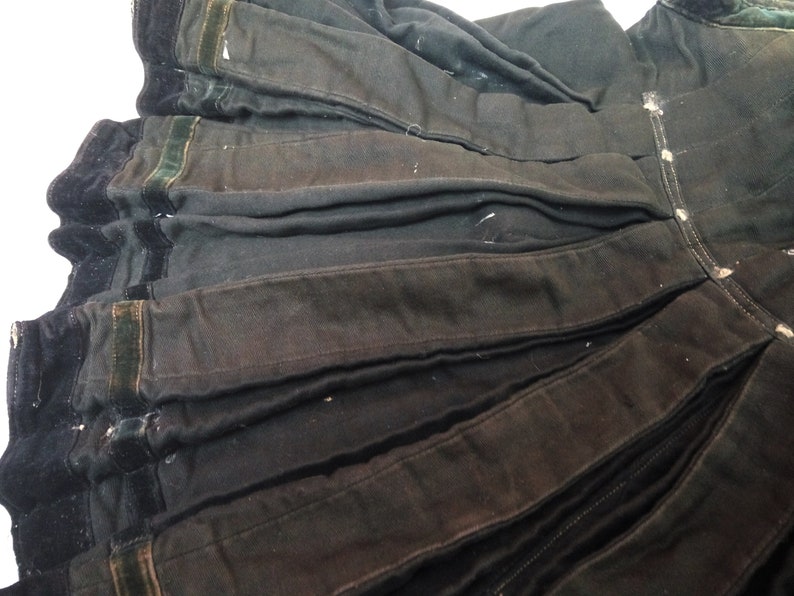 May include: Black skirt with a pleated design and a velvet trim. The skirt has a dark green velvet trim along the bottom edge.