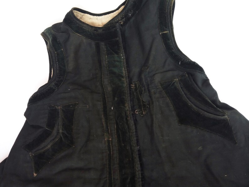 May include: A black sleeveless vest with velvet trim and pockets. The vest has a zipper closure and a stand-up collar.