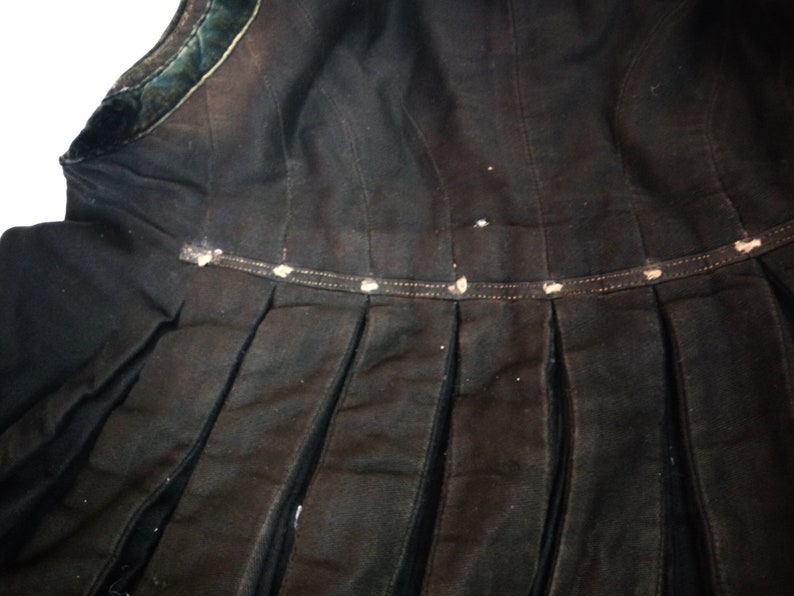 May include: Black skirt with a pleated design and a black velvet trim. The skirt has a waistband with a row of white buttons.
