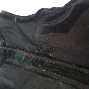 May include: A black vest with green velvet trim and a pocket on the front. The vest has a few metal clasps.