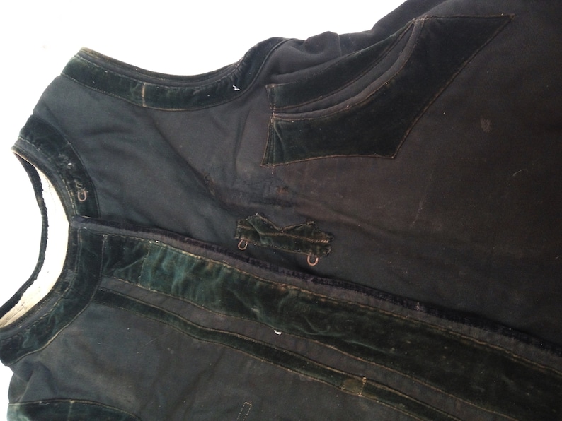 May include: A black vest with green velvet trim and a pocket on the front. The vest has a few metal clasps.