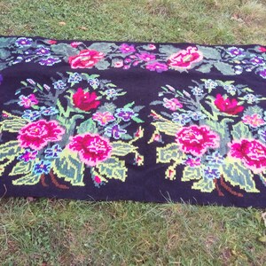 May include: A black wool rug with a floral pattern. The rug features pink, red, green, and blue flowers on a black background.