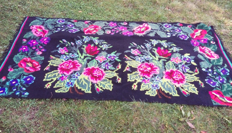 May include: A black wool rug with a floral pattern. The rug features pink, red, green, and blue flowers on a black background.
