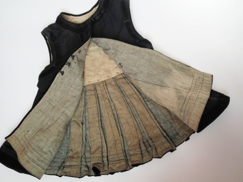 May include: A black velvet dress with a pleated lining. The dress is sleeveless and has a round neckline.