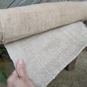 May include: A roll of natural linen fabric, partly unrolled to show the texture. The fabric has a raw edge and a slightly coarse weave. The neutral colour suggests it could be used for various craft projects or home decor.