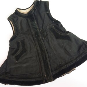 May include: A black velvet vest with a high neckline and a zipper closure. The vest has a flared skirt and is trimmed with black velvet ribbon.