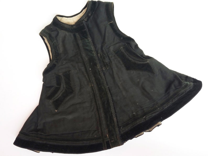 May include: A black velvet vest with a high neckline and a zipper closure. The vest has a flared skirt and is trimmed with black velvet ribbon.