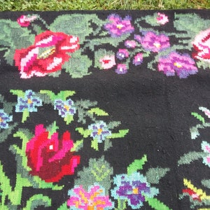 May include: A black wool rug with a floral pattern woven into the fabric. The flowers are in shades of pink, red, blue, and green.