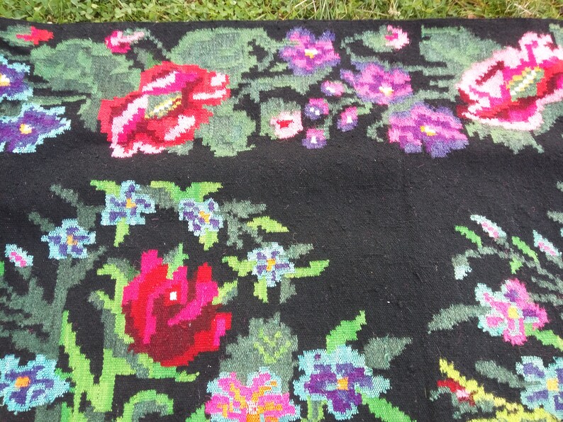 May include: A black wool rug with a floral pattern woven into the fabric. The flowers are in shades of pink, red, blue, and green.