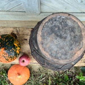 May include: A rustic, dark brown, round, woven basket with a lid sits on a wooden surface with three pumpkins. One pumpkin is orange, one is green and orange, and one is red.
