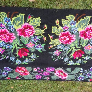 May include: A black wool rug with a floral design. The rug features pink, red, green, blue, and yellow flowers. The rug is hand-woven and has a traditional Romanian design.