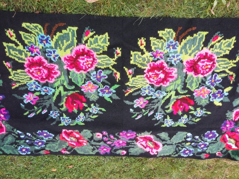 May include: A black wool rug with a floral design. The rug features pink, red, green, blue, and yellow flowers. The rug is hand-woven and has a traditional Romanian design.