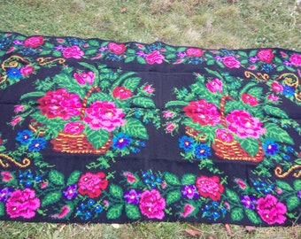 May include: A black wool rug with a floral design. The rug features two baskets filled with pink, red, and white flowers. The flowers are surrounded by green leaves and blue and yellow accents.