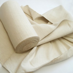 May include: A roll of natural-colored fabric, unrolled and folded, showing the texture of the material.