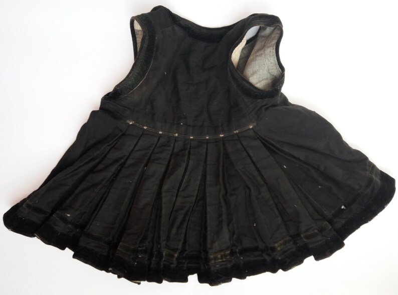 May include: A black sleeveless dress with a pleated skirt and velvet trim. The dress is made of a soft, lightweight fabric.