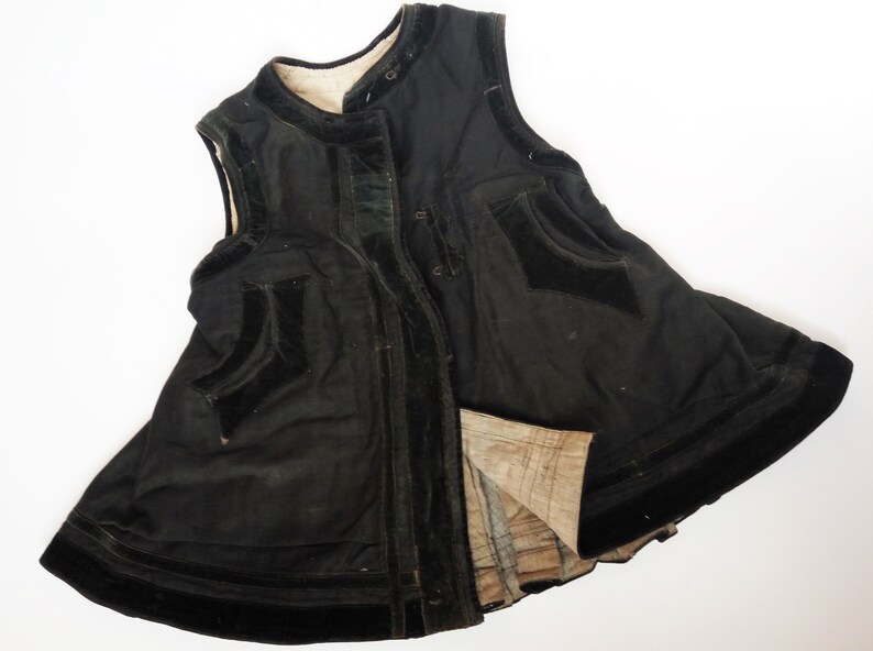 May include: A black sleeveless garment with a velvet trim and a button closure. The garment has a flared skirt and a lining.