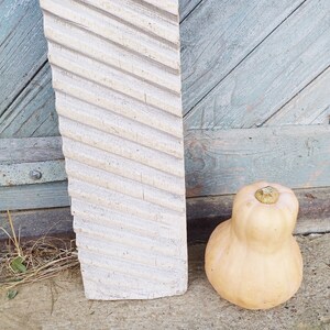 May include: A white wooden washboard with a diagonal pattern, leaning against a weathered blue wooden door. A light brown squash sits on the ground in front of the washboard.