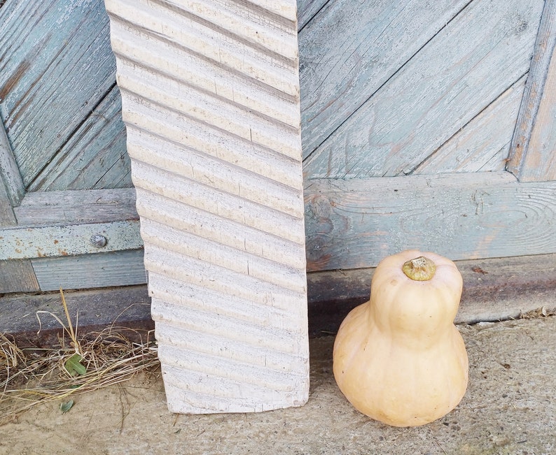 May include: A white wooden washboard with a diagonal pattern, leaning against a weathered blue wooden door. A light brown squash sits on the ground in front of the washboard.