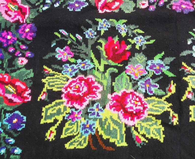 May include: A black rug with a floral pattern. The flowers are red, pink, blue, and green. The rug is made of wool and has a traditional design.