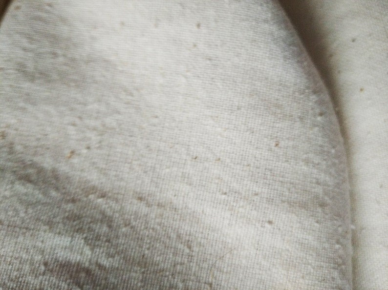 May include: Close-up of a white fabric with a slightly textured surface. The fabric has a few small brown spots.