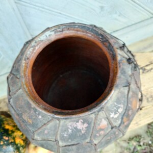 May include: A large, brown, clay pot with a woven pattern around the rim. The pot has a wide opening and is made of a rough, textured material.