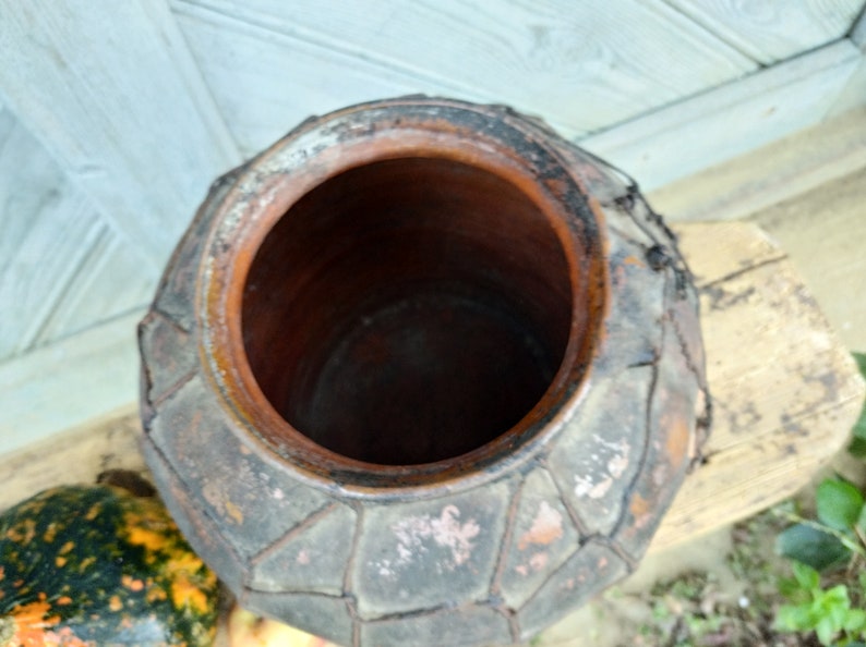 May include: A large, brown, clay pot with a woven pattern around the rim. The pot has a wide opening and is made of a rough, textured material.