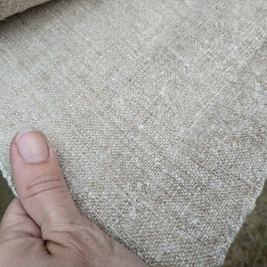 May include: Close-up of natural linen fabric. The fabric has a textured weave and a neutral beige colour. The edge of the fabric is visible, showing its raw, unfinished state. Ideal for sewing, crafting, or home decor projects.