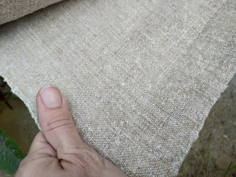 May include: Close-up of natural linen fabric. The fabric has a textured weave and a neutral beige colour. The edge of the fabric is visible, showing its raw, unfinished state. Ideal for sewing, crafting, or home decor projects.