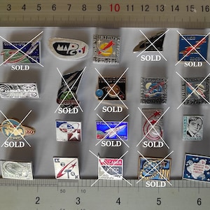 May include: A collection of 15 vintage Soviet space program enamel pins. The pins feature various designs, including rockets, satellites, astronauts, and the text "MAP-1".