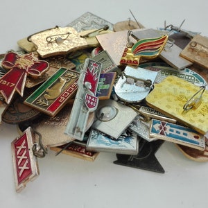 Może przedstawiać: Kolekcja vintage emaliowanych znaczków z różnymi wzorami, w tym czerwoną kokardą z 1917 roku, zielonym i żółtym ptakiem z napisem "ZSRR" oraz czerwono-białym znaczkiem z lat 1941-1945.