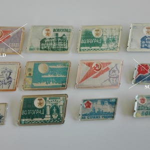 Puede incluir: Una colección de pines de esmalte vintage con varios diseños, incluyendo una estrella roja, un barco y el texto "Volgograd". Algunos pines están marcados como "Vendido".