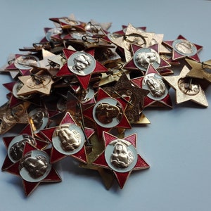 K&ouml;nnte beinhalten: Eine Sammlung von sternf&ouml;rmigen Vintage-Anstecknadeln. Die Anstecknadeln haben einen roten Emaille-Rand, ein zentrales Medaillon mit einem Reliefportr&auml;t und eine Anstecknadel. Die Anstecknadeln sind in verschiedenen Gold- und Silbert&ouml;nen gehalten.