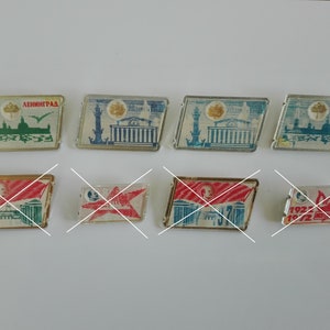 Puede incluir: Una colección de ocho pines de esmalte vintage con diferentes diseños. Los pines son rectangulares y presentan imágenes de edificios, banderas y otros símbolos. Los pines son de varios colores, incluyendo rojo, azul, blanco y verde.