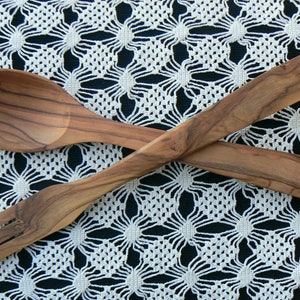 May include: A wooden salad serving set with a spoon and fork. The utensils are crossed and laid on a white crocheted tablecloth.