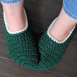 May include: A pair of green crocheted slippers with white trim. The slippers are made with a textured stitch and have a pointed toe.