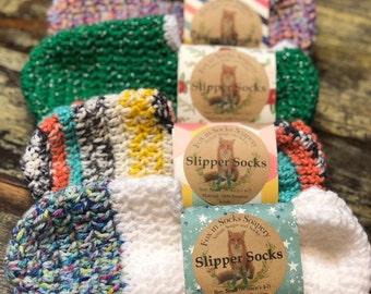 May include: Four pairs of colorful crocheted slipper socks with white trim. Each pair is packaged with a label that reads "Fox in Socks Soapery" and "Slipper Socks". The label also includes the size and material information.