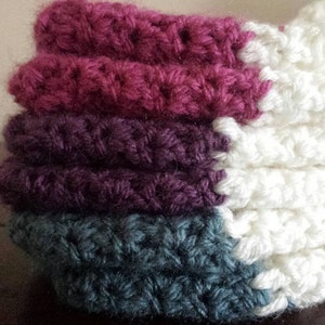 May include: A stack of crocheted fabric squares in shades of pink, purple, and teal. The squares are joined together to create a larger piece of fabric.
