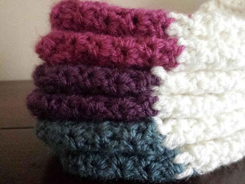 May include: A stack of crocheted fabric squares in shades of pink, purple, and teal. The squares are joined together to create a larger piece of fabric.