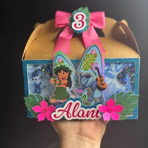 May include: A custom-made birthday gift box featuring Lilo & Stitch characters. The box is brown with a blue glitter frame, pink flowers, and a pink bow with the number 3. The name "Alani" is displayed on the front.
