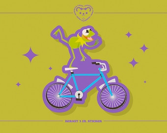 May include: A green frog character riding a blue bicycle with purple wheels. The frog is wearing a white shirt and a red bow tie. The bicycle has a purple frame and a white seat. The image is a 3-inch sticker with the text "Kermit 3 in. sticker".
