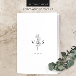 May include: A white folded wedding program with a black floral design and the initials "V & S" and the date "05.06.21".