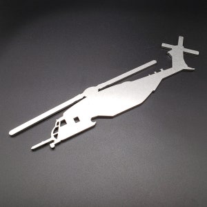 May include: A silver metal silhouette of a helicopter. The helicopter is facing right and has a long tail rotor.