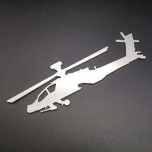 May include: A silver metal silhouette of an Apache helicopter. The helicopter is facing right and has a detailed design.
