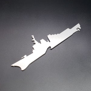 May include: A silver metal keychain shaped like a silhouette of a warship. The keychain is a simple design with a smooth, polished finish.