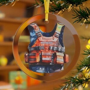 May include: A round glass ornament with a watercolor painting of a safety vest with the name "WITHERS" printed on it.